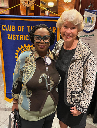 Ada and Nancy smile as they stand in front of a club banner.