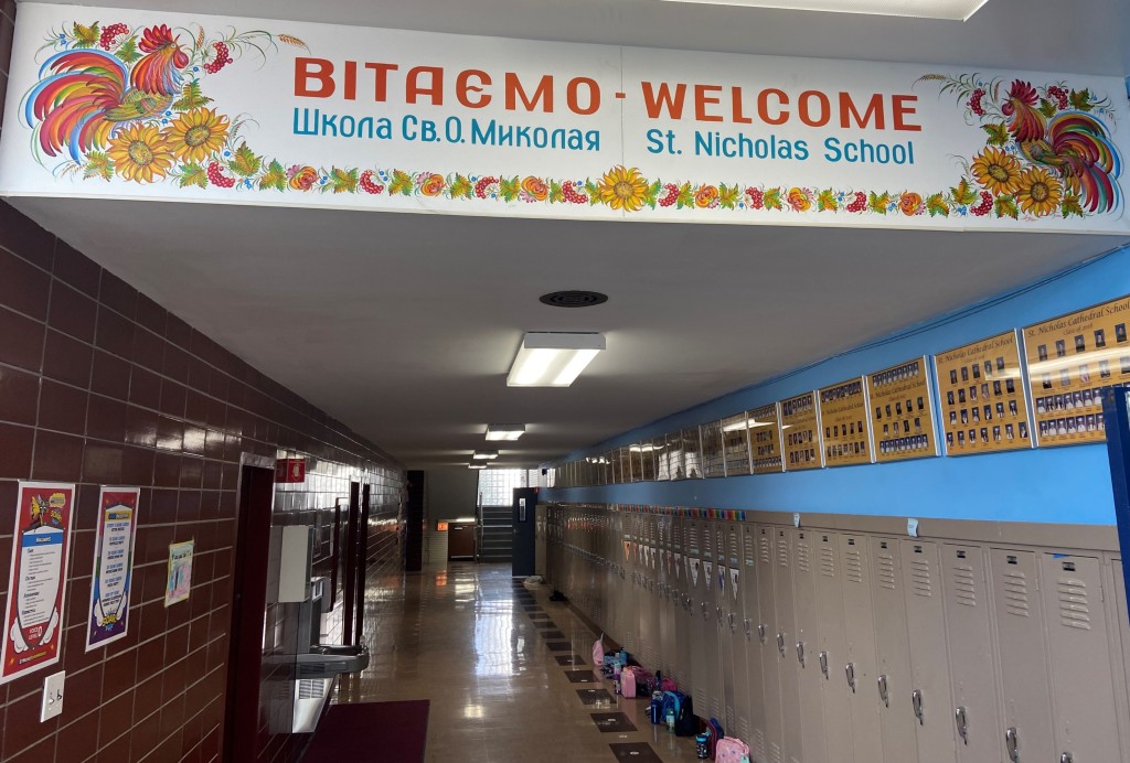 Large decorative sign over a school hallway lined with lockers.