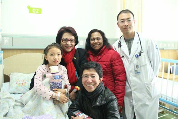 A child holds a doll in a hospital bed, behind her are the child's parents and doctor