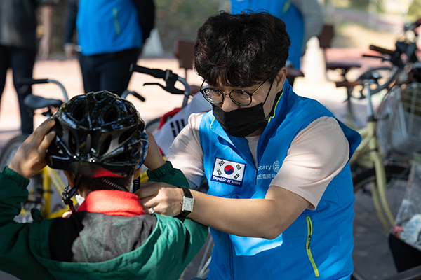 A Rotary member in a blue vest adjusts the helmet for a visually-impaired rider.