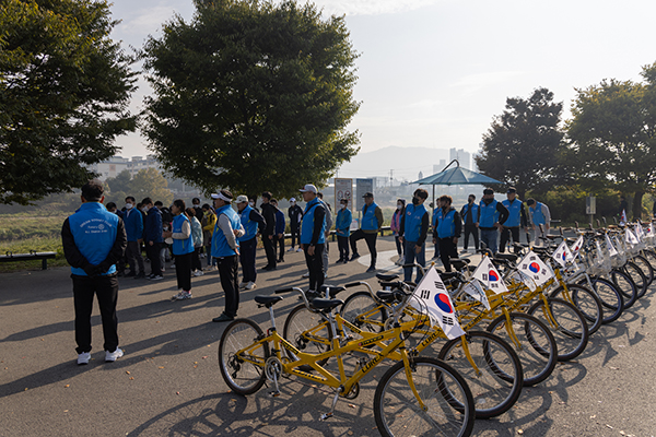 A group of Rotary members and volunteers stand in a group in front of a row of tandem bikes.