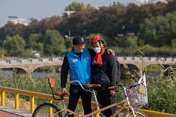 A Rotary member in a blue vest has his arm around the shoulder of a visually-impaired resident in a red bike helmet during a break in the ride.