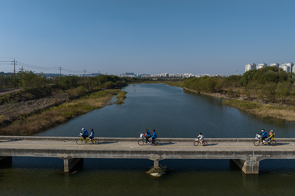 Tandem bicycle riders cross a bridge over the river.