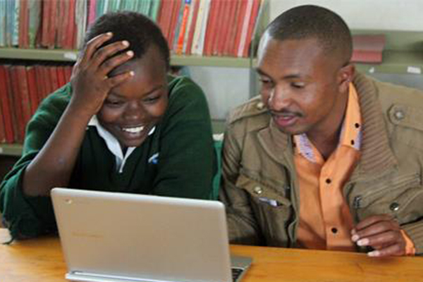 Two male teachers look at the screen of a laptop open in front of them