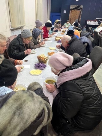 A dozen people in coats eat donated food