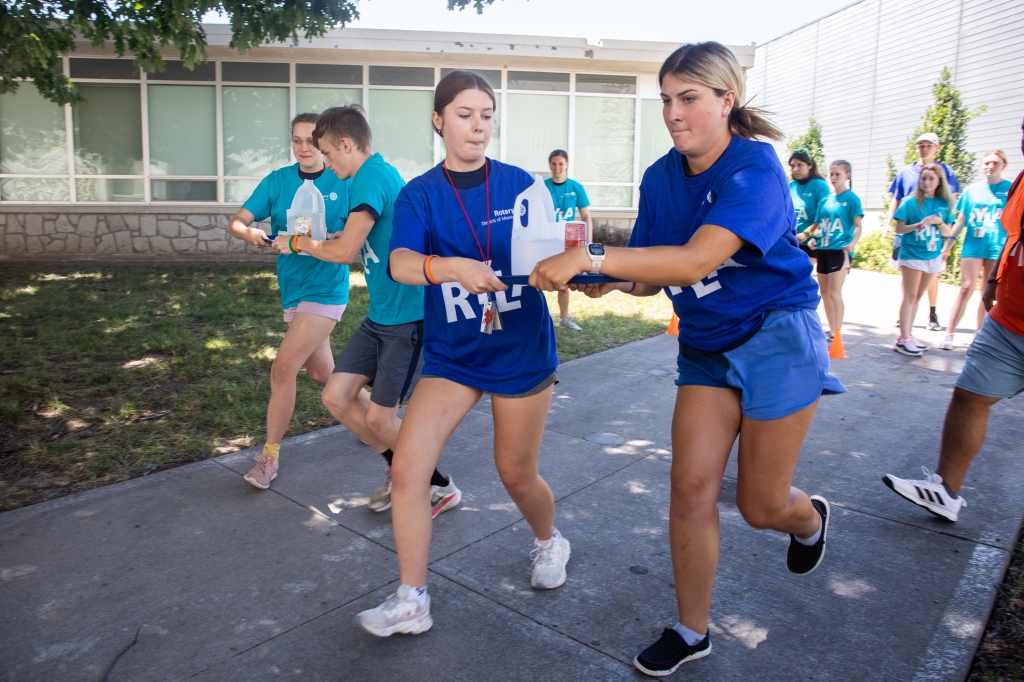 Two young women run while balancing a tray of water