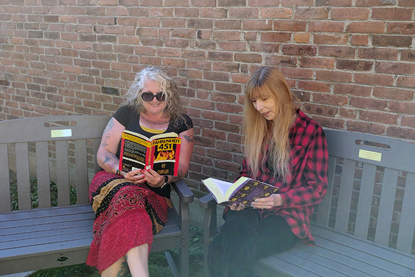 Two women read books on benches made from recycled materials.