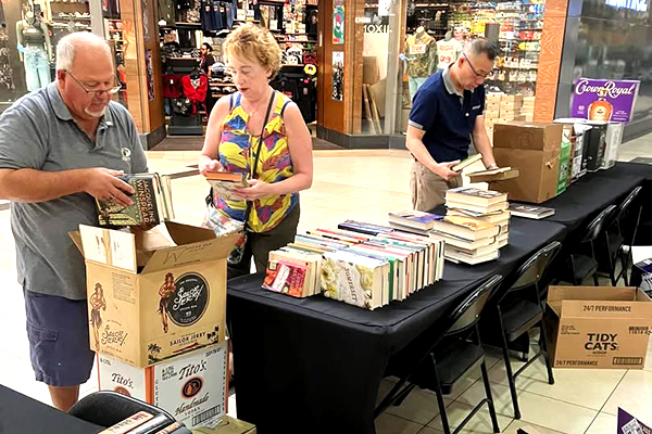 three club members arrange books on a table for a book sale
